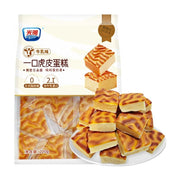 光明一口小虎皮蛋糕牛乳味包装袋，展示了内部独立包装的蛋糕块和一盘切成方块的虎皮蛋糕，包装上标有0反式脂肪酸和2.1倍牛乳蛋白。