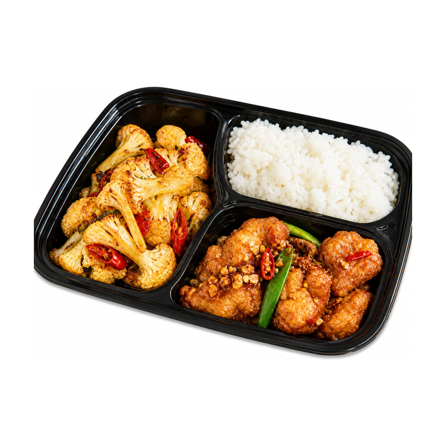 黑色三格便当盒内装有干锅花菜、椒盐鸡块和白米饭，白色背景。