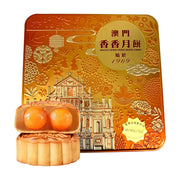 澳门香香双黄白莲蓉月饼礼盒，金色铁盒包装印有大三巴牌坊图案，前方展示切开的月饼，露出两颗饱满的咸蛋黄。