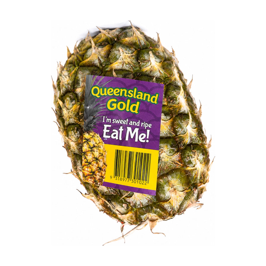 一颗完整的昆士兰黄金菠萝，带有紫色标签，标签上印有 Queensland Gold, I'm sweet and ripe Eat Me! 字样及条形码。