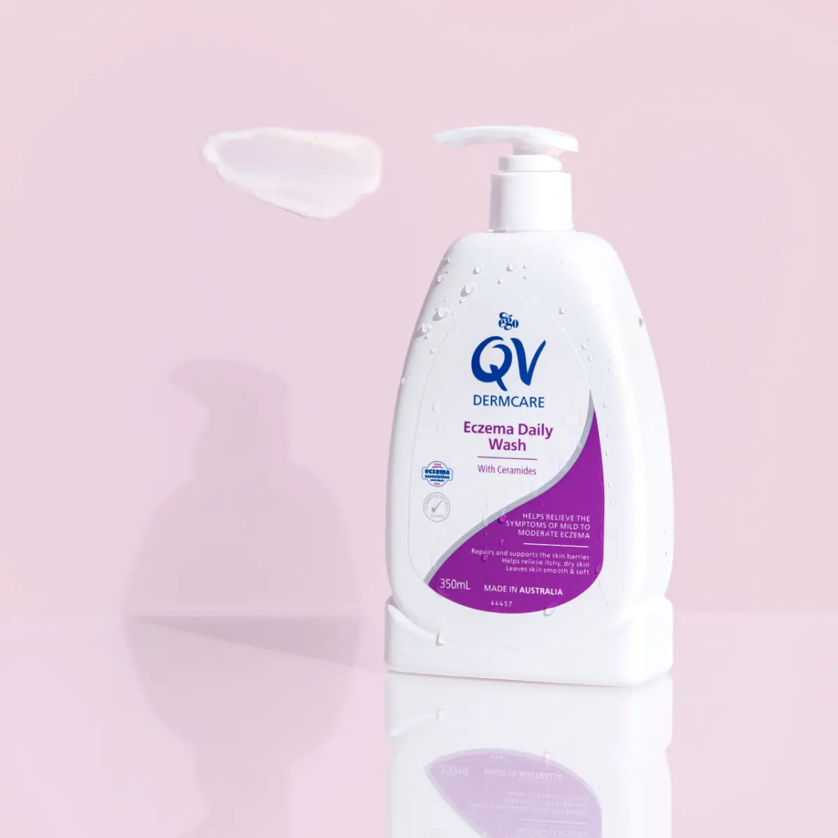 QV 沐浴露粉色背景展示图，瓶身带水珠，左上角有白色乳液质地涂抹效果