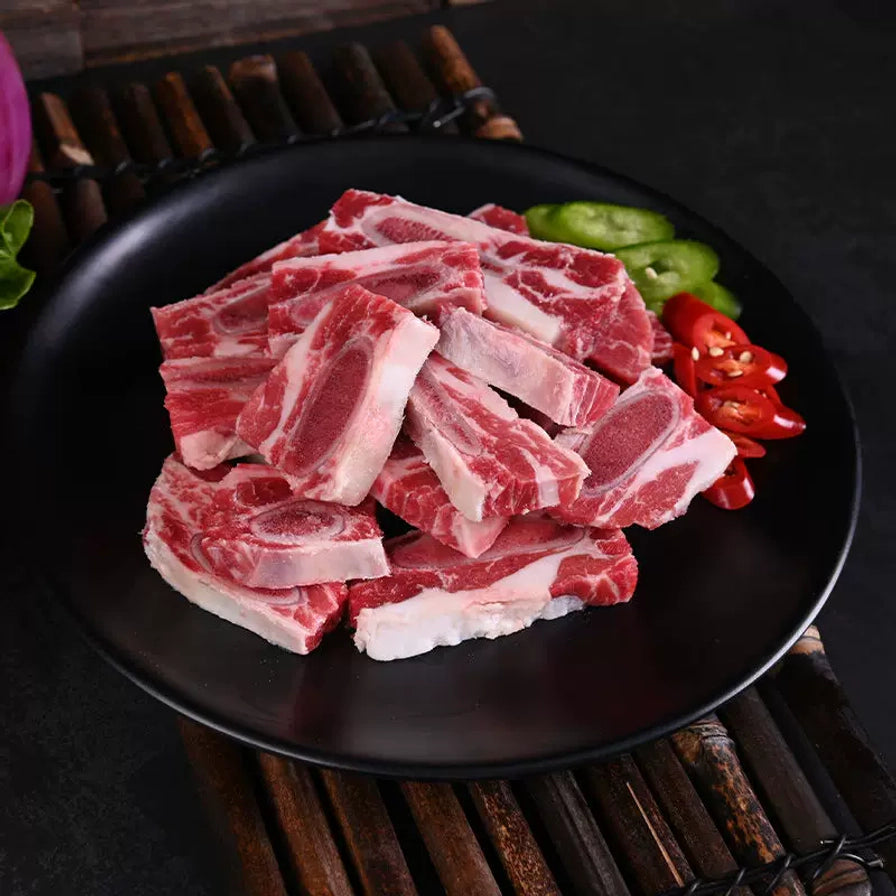 黑色圆盘中盛放的切块和牛牛仔骨，配有青红辣椒圈装饰，背景为深色竹帘。
